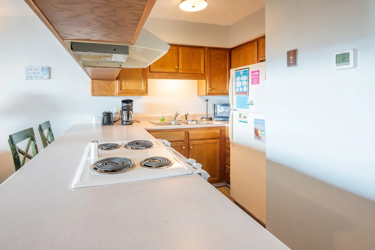 A kitchen area with a countertop, stove, kitchen cabinets, coffee maker, and refrigerator. The layout encourages morning routines like brewing coffee or sharing breakfast and provides a backdrop for holiday baking or social gatherings.