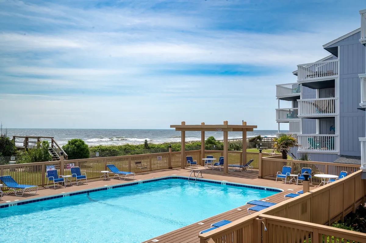 This image captures the Sea Colony's inviting oceanfront swimming pool surrounded by lounge chairs, with sweeping views of the ocean in the background. A pergola provides shaded seating, and the mood is tranquil and leisurely, perfect for both relaxation and socializing on sunny days.