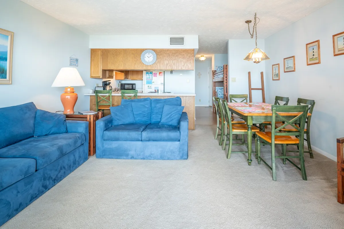 A welcoming living area with blue sofas, a dining table, kitchen area, and wall art. The main sofa can function as a sleeper, and the space encourages family gatherings and relaxation after a day of adventures.