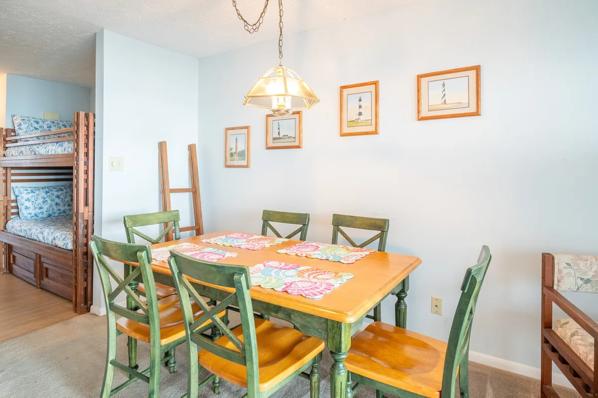 A warm, inviting interior scene showing a dining table set near bunk beds and decorated with lighthouse pictures. The setup speaks to flexible sleeping arrangements and communal family time, reinforcing the condo’s suitability for families.